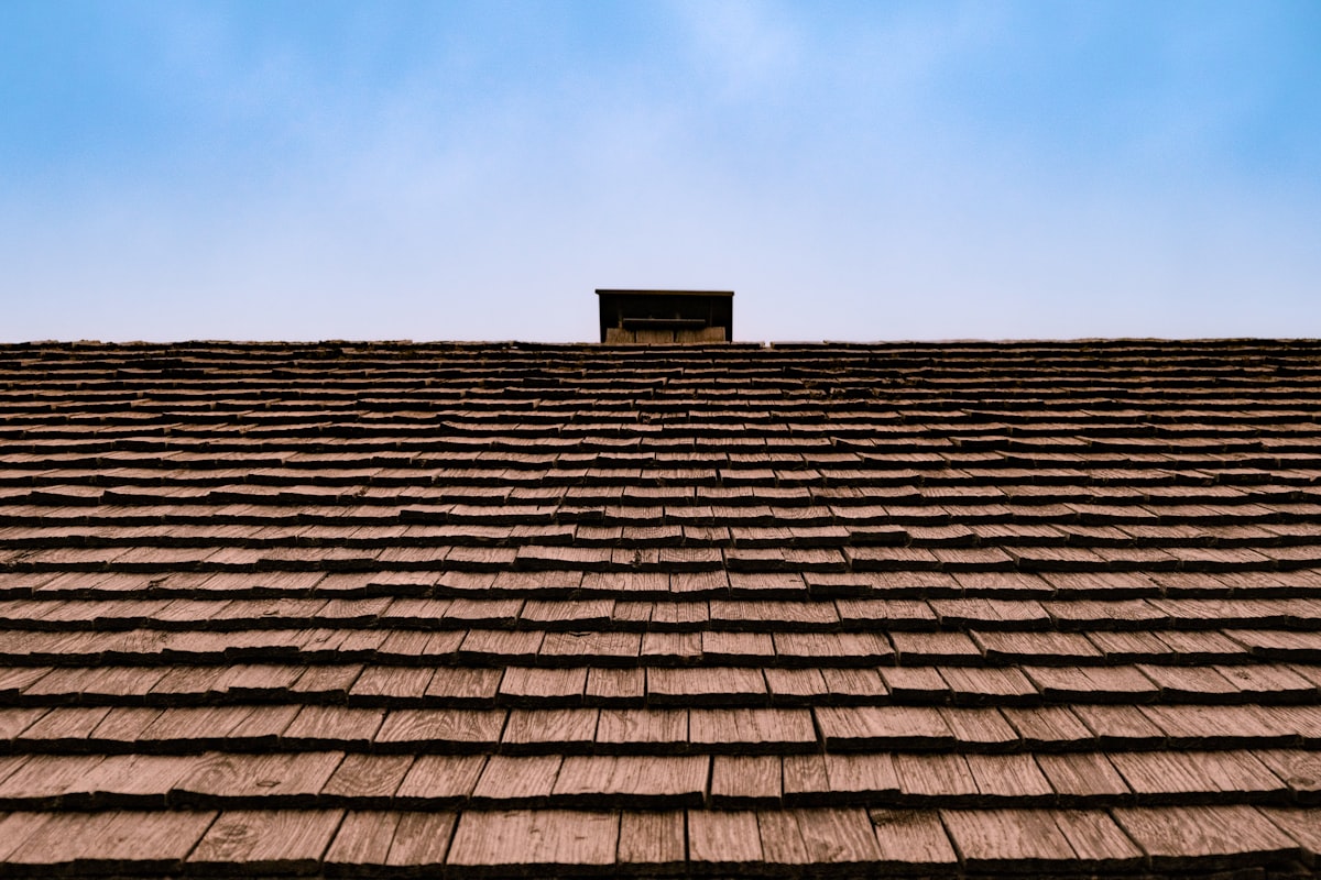 Steep wooden shingle roof against blue sky with small vent box